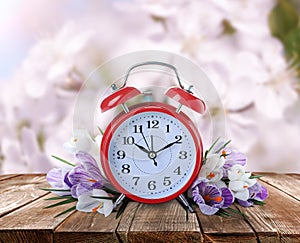 Alarm clock and spring flowers on wooden table. Time change