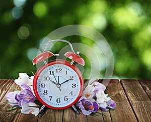 Alarm clock and spring flowers on wooden table. Time change