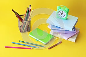 Alarm clock, stack of books and stationery on yellow background, back to school, holidays, education