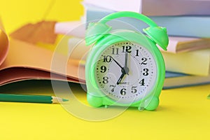 Alarm clock, stack of books and stationery on yellow background, back to school, holidays, education