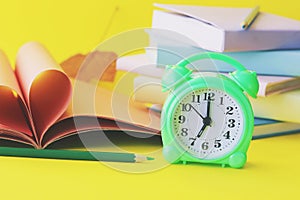 Alarm clock, stack of books and stationery on yellow background, back to school, holidays, education