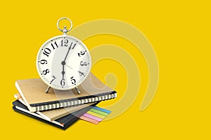 Alarm clock stacked on brown and black notebook with a post it note paper. Isolated on yellow background with copy space and clipp