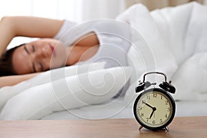 Alarm clock standing on bedside table has already rung early morning to wake up woman in bed sleeping in background