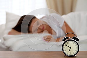 Alarm clock standing on bedside table has already rung early morning to wake up woman in bed sleeping in background