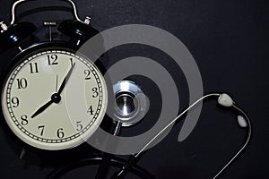 Alarm clock, stethoscope on black background