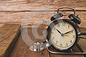 Alarm clock and stethoscope on wooden board. Conceptual image