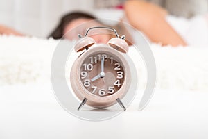 Alarm clock on the table in the bedroom. Peaceful model trying to wake up lying on her bed, selective focus. copy space