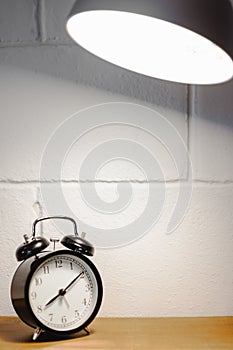 Alarm clock on table with lamp and blurred white brick