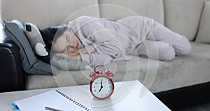 A alarm clock on table wakes up a woman sleeping on couch