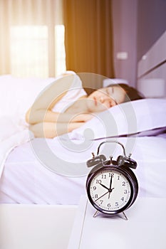 Alarm clock on table and woman sleeping on bed in bedroom
