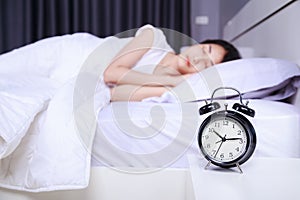 Alarm clock on table and woman sleeping on bed in bedroom