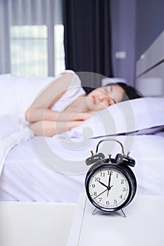 Alarm clock on table and woman sleeping on bed in bedroom