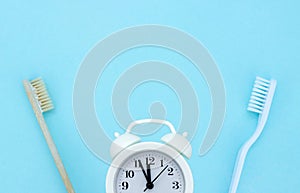 Alarm clock, toothbrushes on light blue background. Healthy teeth. Morning routine concept. Care for oral and dental care concept