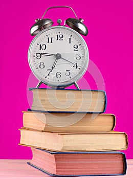 Alarm clock on top of piles of books on yellow background.