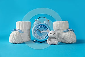 Alarm clock, toy bear and baby booties on light blue background. Time to give birth