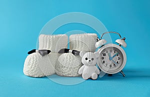 Alarm clock, toy bear and baby booties on light blue background. Time to give birth