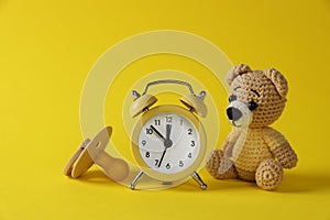Alarm clock, toy bear and baby dummy on yellow background. Time to give birth