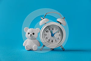 Alarm clock and toy bear on light blue background. Time to give birth