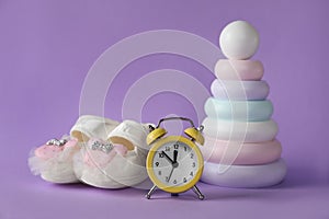 Alarm clock, toy pyramid and baby booties on violet background. Time to give birth