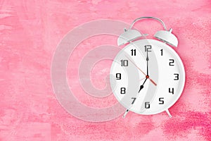 Alarm clock with twin bells and ringer showing 7 seven o'clock on pink background