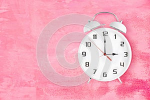 Alarm clock with twin bells and ringer showing 3 o'clock on pink background photo