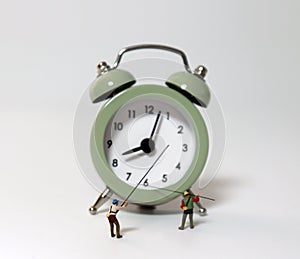 An alarm clock and two miniature men holding fishing rod.