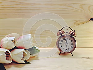 Alarm clock and white flowers in pink vase on brown wood table