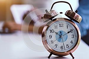 Alarm clock on white table background with businessman working with laptop.Time management and punctuality at work concept