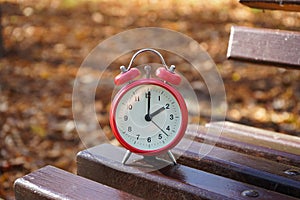 Alarm clock on a wooden bench in the autumn park. The concept change time