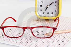 Alarm clock,wooden pencil and glasses on filled exam sheet on white surface