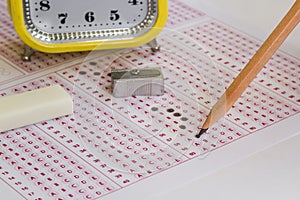 Alarm clock,wooden pencil and rubber on filled exam sheet,
