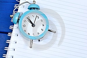 Alarm clock on wooden table with empty notepad