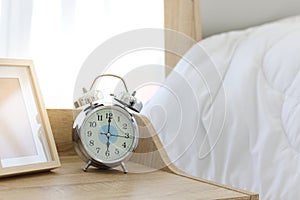 Alarm clock on wooden table in the white bedroom at six o`clock in the morning