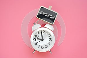 Alarm clock and word menopause on a pink background photo