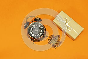 Alarm o`clock showing 7 o`clock and autumn leaves, gift box isolated on orange background. time to holidays