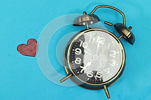 Alarm showing 7 o`clock with wooden heart isolated on blue.
