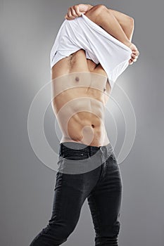 Alarm, youve failed me. Studio shot of a muscular young man getting undressed against a grey background.