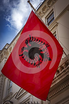 Albanian flag hanging outside grand residence under cloudy sky