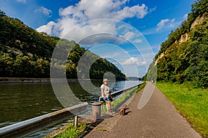 Albert canal between two rocky mountain slopes, senior adult tourist together with her dachshund taking a break