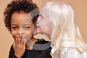 Albino girl tells a secret in the ear of multiracial african boy