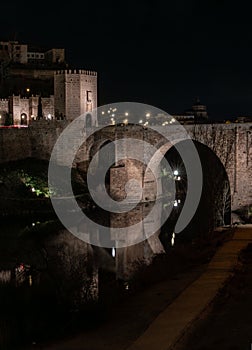 Alcantara Bridge with the tower at the entrance to the city and its reflection in the Tagus River in the middle of the night.