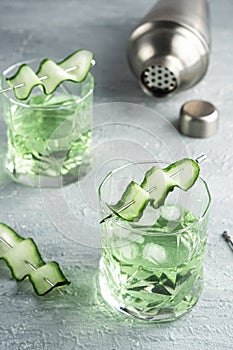 Alcohol cocktail with cucumber pouring from shaker in whiskey glass with ice cubes. Summer coctail