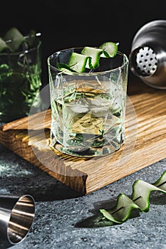 Alcohol cocktail with cucumber in whiskey glass with ice cubes. Summer spirit drink and shaker