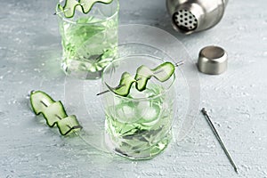 Alcohol cocktail with cucumber in whiskey glass with ice cubes. Summer spirit drink and shaker