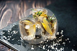 Alcohol cocktail with ice and smoking rosemary on dark table lemon