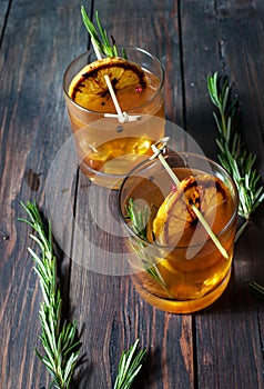 Alcohol cocktail with lemon, ice and smoking rosemary on dark table