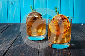 Alcohol cocktail with lemon, ice and smoking rosemary on dark table.