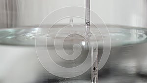 alcohol distilling process closeup - liquid distilled transparent liquid flowing in large glass jar with floating