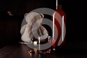Alcohol and divorce concept. Teddy bear, rings and bottle with glass on wooden table