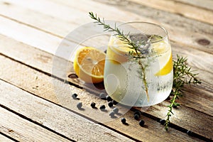 Alcohol drink gin tonic cocktail with lemon, juniper branch,  and ice on rustic wooden table